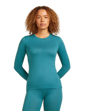 Woman wearing an Icebreaker Oasis teal  long-sleeve top on a white background