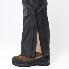 View of Montbell Men's Ultralight Black DryTec Rain Pants zipper on lower leg  of a man while wearing boots on a white background
