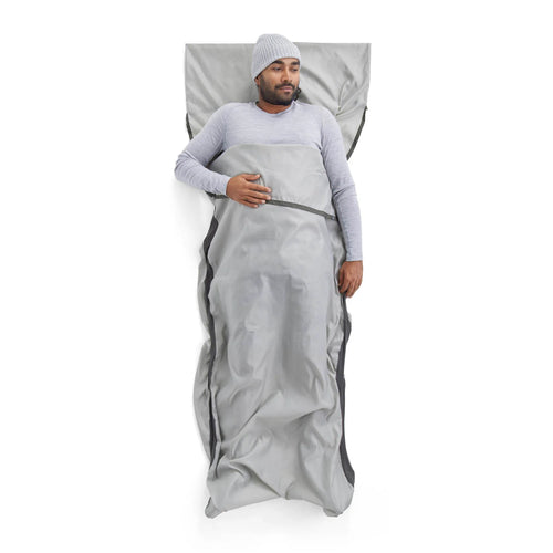 Man lying on a gray sleeping bag liner against a white background