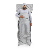 Man lying on a gray sleeping bag liner against a white background